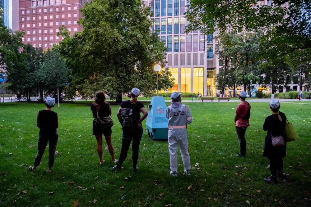 Eine Gruppe von Menschen in einem öffentlichen Park, im Hintergrund sind Hochhäuser sichtbar