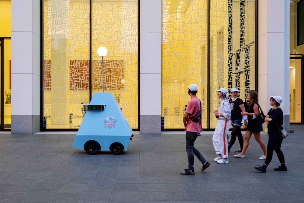 Eine Gruppe von Menschen wird von einem fahrbaren Roboter an einer hell beleuchteten Unternehmenslobby vorbeigeführt